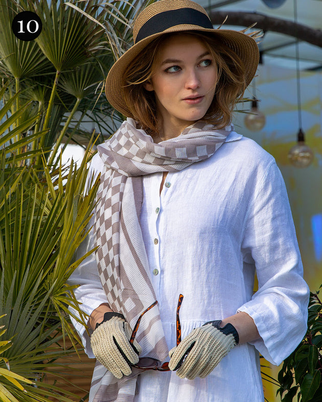 Woman wearing crochet-back imitation peccary leather gloves in black with a check scarf and straw hat at a resort