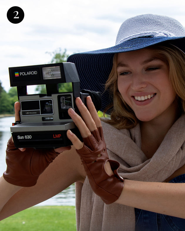 Woman wearing straw floppy hat in white/navy with leather fingerless gloves in the park