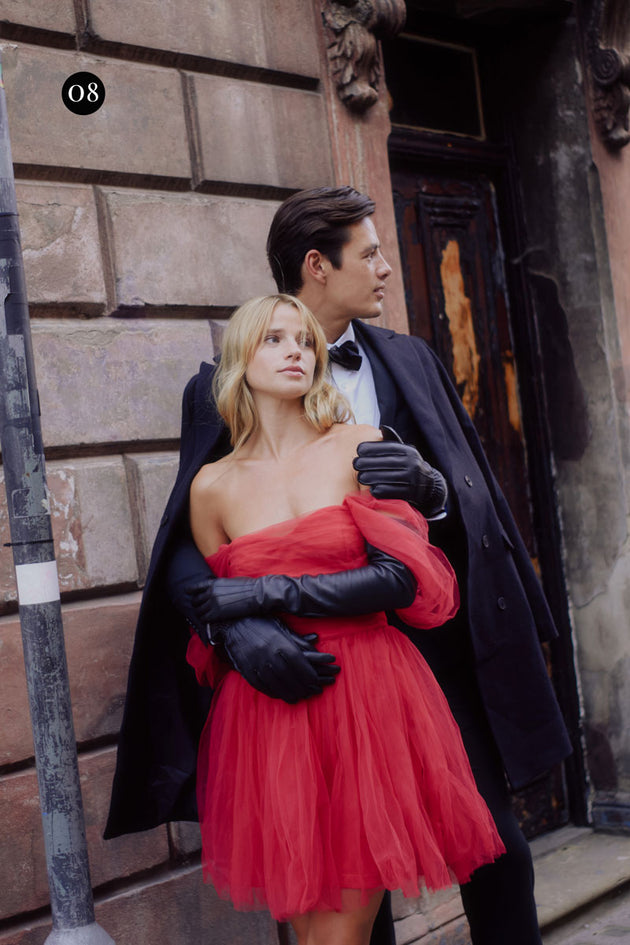 woman wearing long opera leather gloves in black and a pink sleeveless dress, man is wearing a three piece suit with black leather gloves