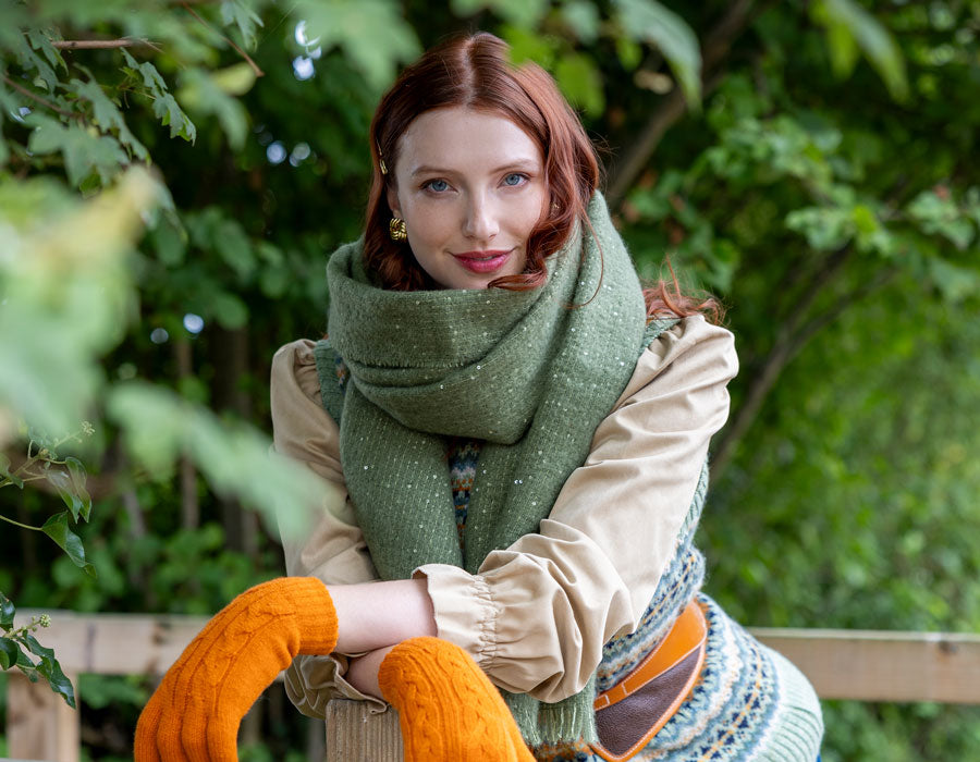 Woman wearing cosy sparkly scarf in green with orange gloves on a walk