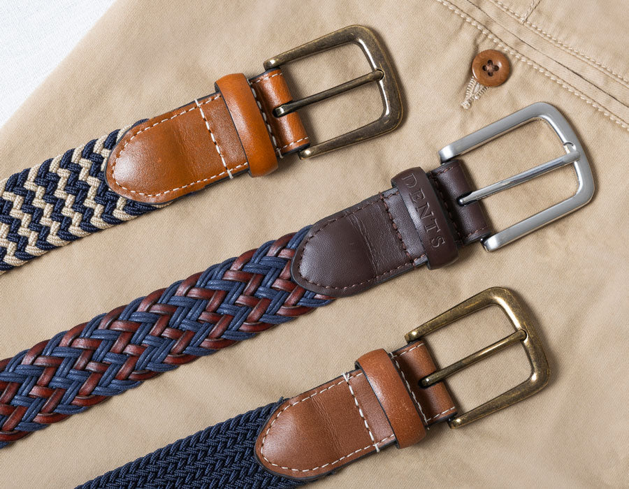 Three woven belts with metal buckles on a beige pair of trousers.