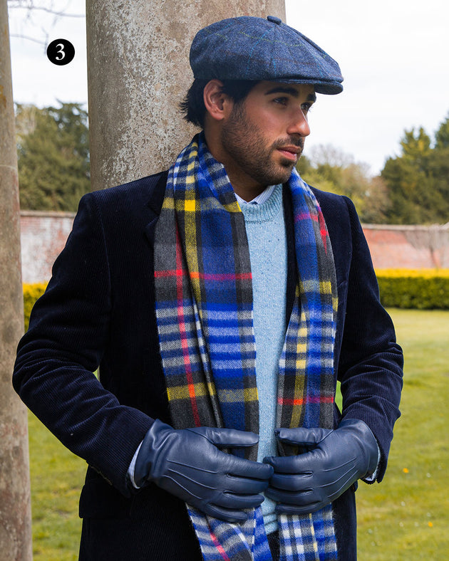 Man wearing heritage bold check cashmere scarf with tassels in night sky, with a tweed hat and leather gloves in the park