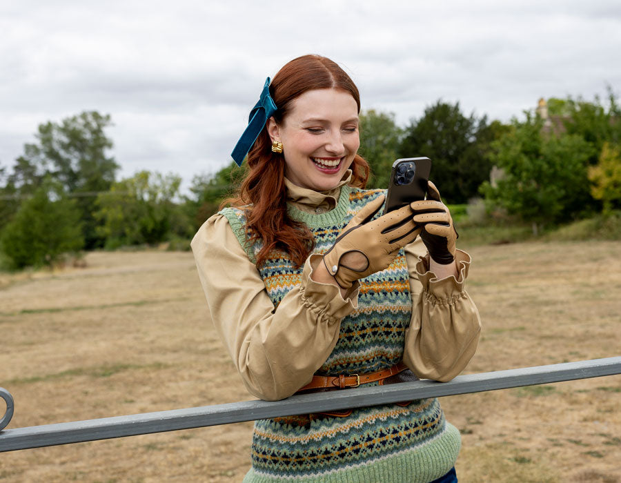 a woman wearing touchscreen leather driving gloves in toffee using her mobile phone outdoors